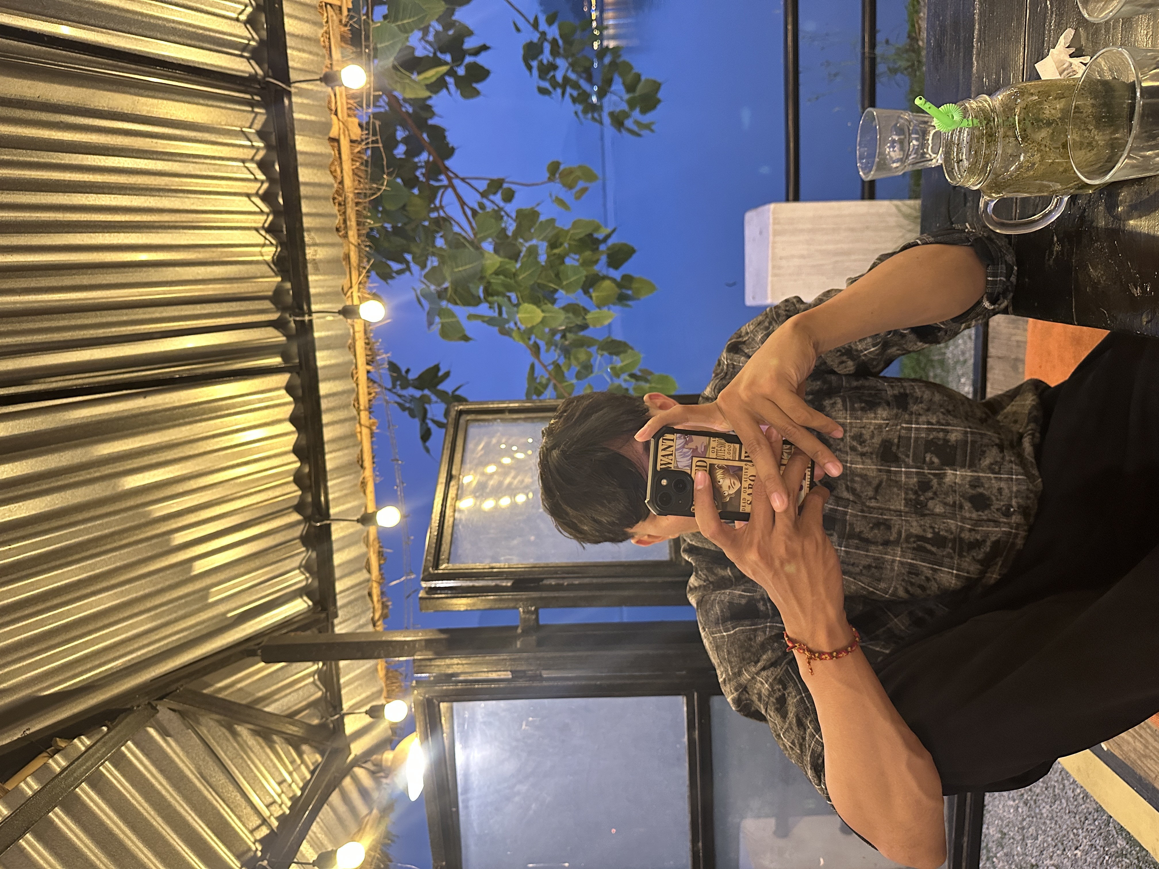 Portrait of Sagar Pun seated in a cafe holding a phone in front of his face